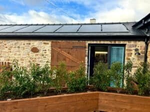 Solar panels on rustic stone cottage with vibrant garden, eco-friendly energy and picturesque setting.
